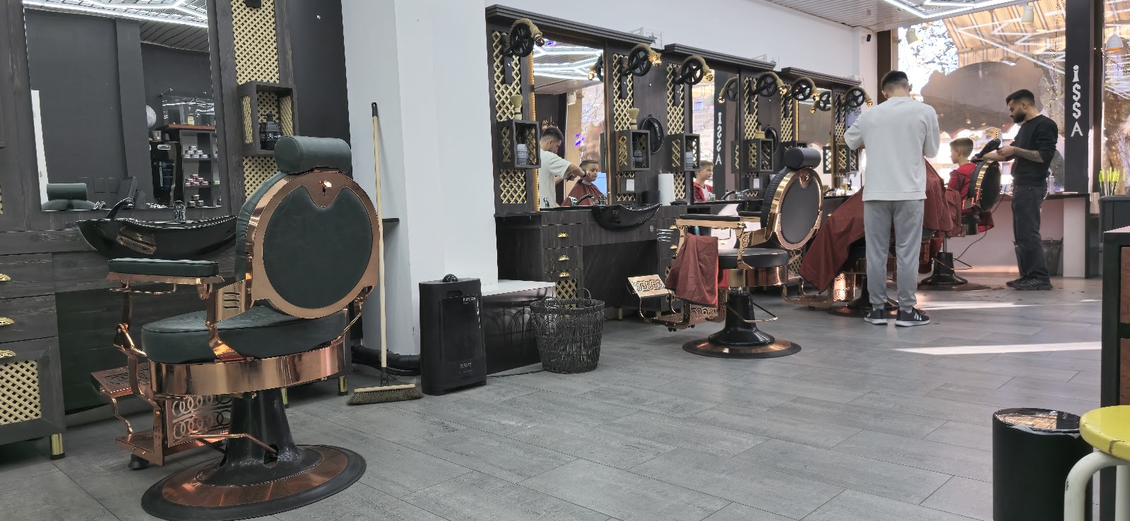 Interieur du salon Issa Barbershop a Bulle - fauteuils barbier cuivre et bronze, barbiers au travail, ambiance soignee